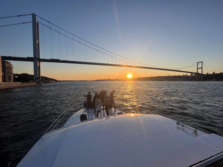 Gäste am Bug einer privaten Yacht bei der Annäherung an die Bosporus-Brücke zum Sonnenuntergang
